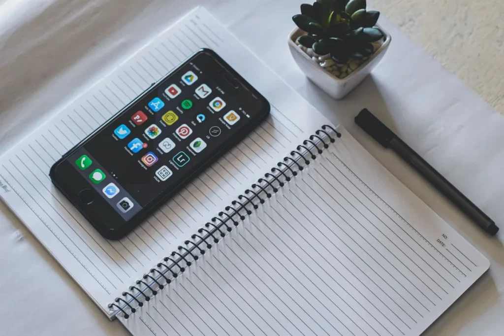Meja kerja dengan ponsel dan buku catatan saat merencanakan caption Instagram