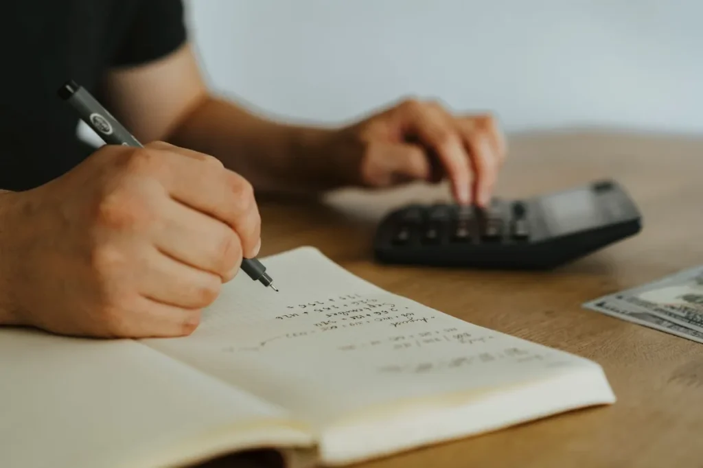 Copywriter menghitung tarif dasar proyek dengan kalkulator dan catatan kerja
