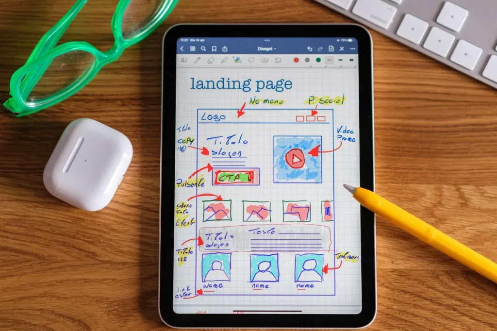 Kerangka landing page digambar di kertas di samping laptop.